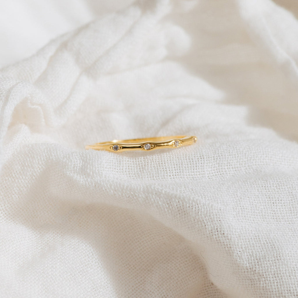 The Juliet Diamond Ring, featuring delicate diamonds, rests on a soft white fabric background, radiating minimalist charm and elegance.