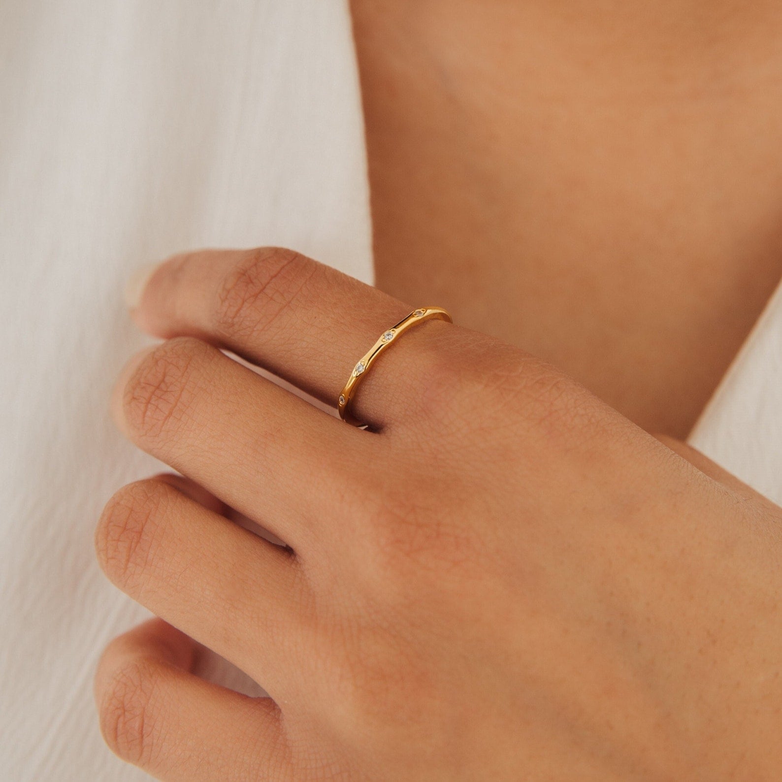 A hand adorned with the Juliet Diamond Ring, a minimalist and dainty design, rests gently on a chest clad in a white garment.