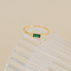 The Empire Emerald Ring features a rectangular green emerald accented with small diamonds, showcased elegantly on a clear ribbed surface.