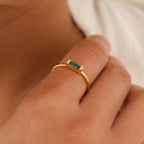 A person wearing the Empire Emerald Ring, a stylish gold band.