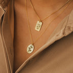 Two Oval Flower Necklaces in rose gold with floral pendants are worn over a beige button-up shirt—elegant, personalized jewelry and a meaningful gift for her.