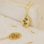 Two Oval Flower Necklaces with delicate floral engravings rest on a light, textured surface with scattered petals, showcasing unique flower jewelry.