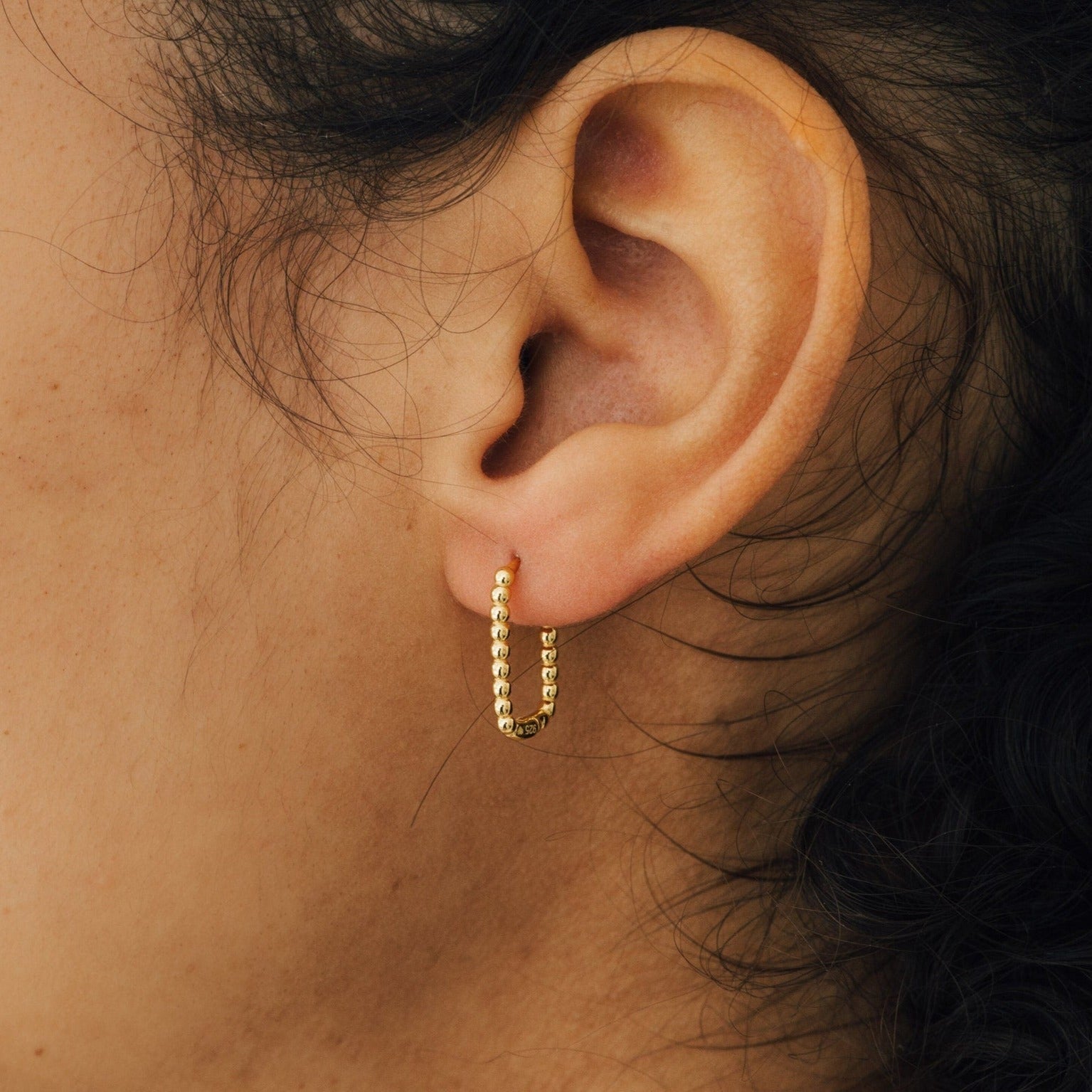 A close-up of an ear adorned with the Indiana Beaded Hoops, small gold hoops perfect for anyone who loves chic earrings with a touch of elegance.