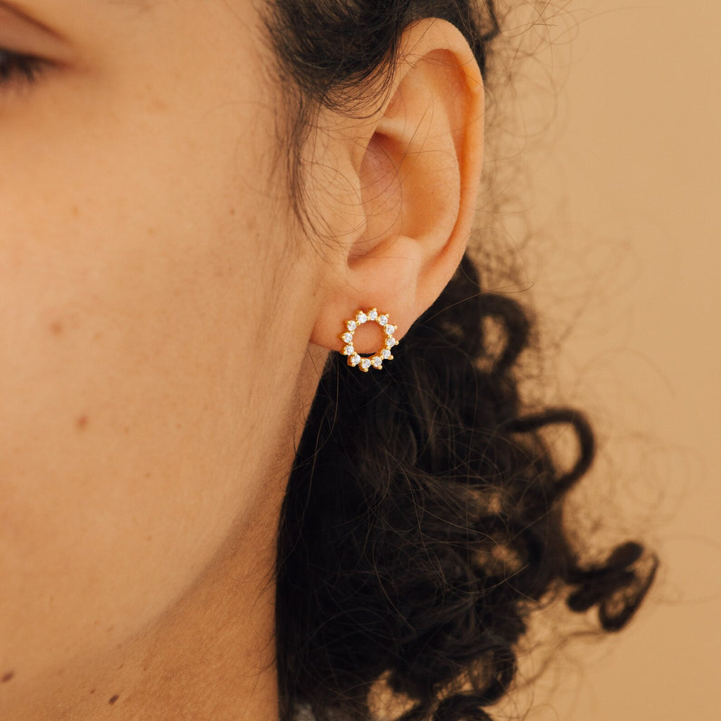 Close-up of a person wearing Helen Diamond Sun Studs, featuring gold with small white stones, set against a beige background.