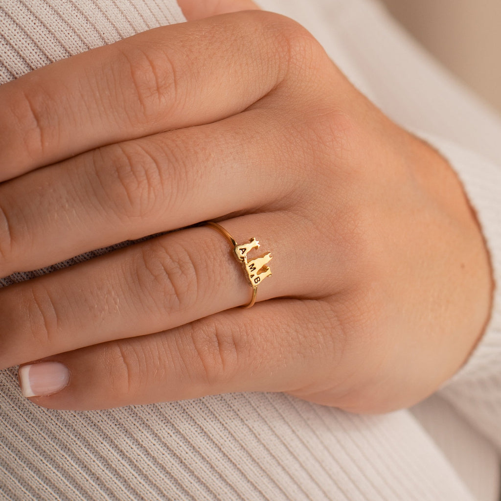 A Pet Initial Ring with a skyline design is shown on a finger against ribbed, light fabric—a personalized jewelry piece ideal for pet lovers.