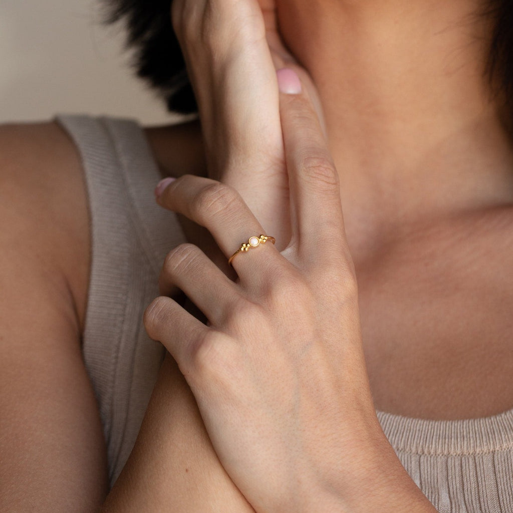 A woman in a beige tank top touches her neck while wearing the Sophia Opal Ring, a vintage-inspired piece featuring delicate small round details.