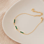 The Malachite Bar Bracelet is a dainty gold chain with three rectangular green malachite stones, ideal for adding a subtle boho charm. Shown displayed on a white plate.