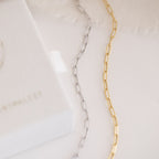 Close-up of a silver and gold Paperclip Chain Bracelet on a white surface with textured fabric in the background—perfect for stacking or pairing with your favorite dainty charms.