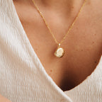 The Earth Locket Necklace shines on someone in a textured white V-neck blouse, adding natural charm to their look.