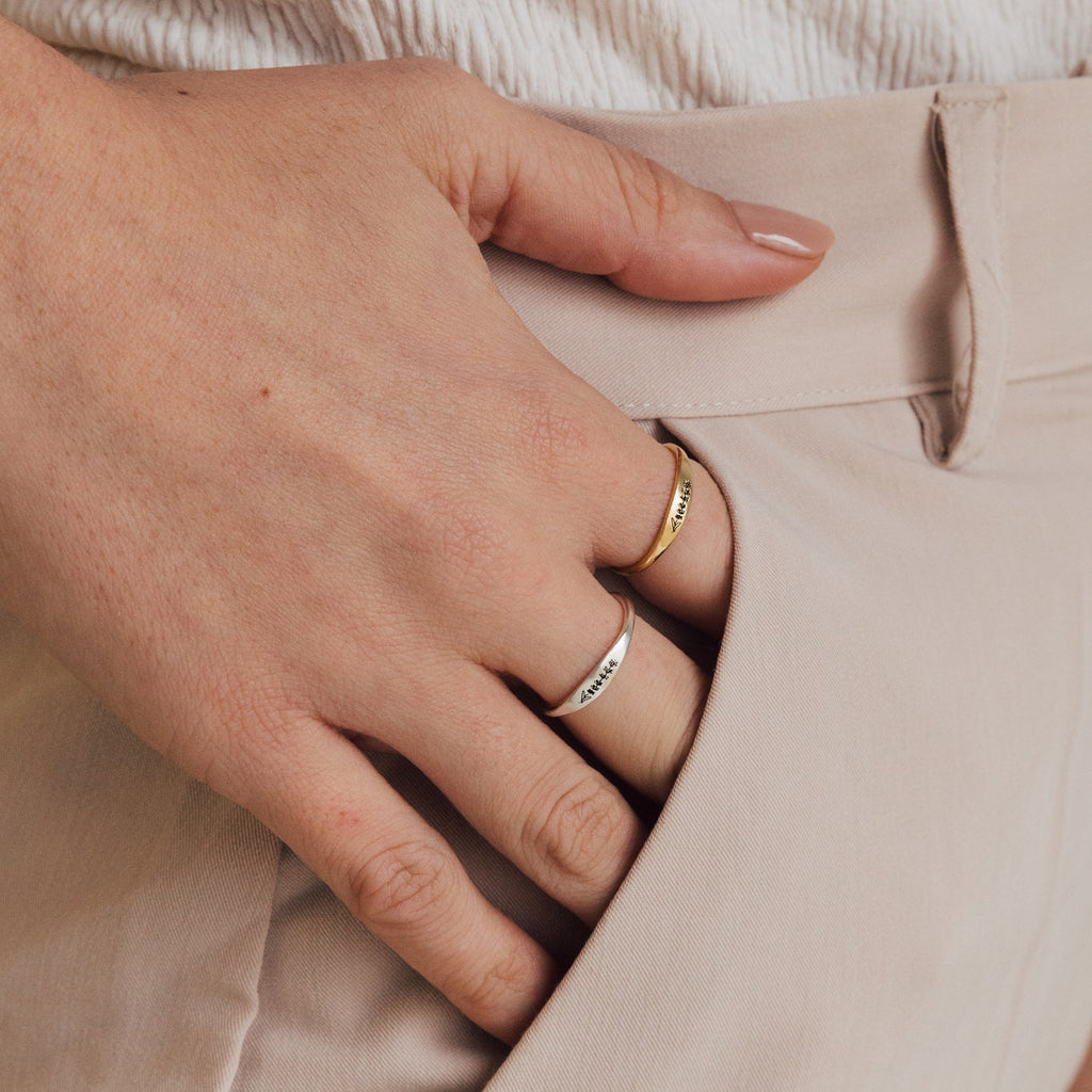 A hand wearing the Skinny Flower Ring, a delicate gold botanical jewelry piece, rests in the pocket of beige pants.