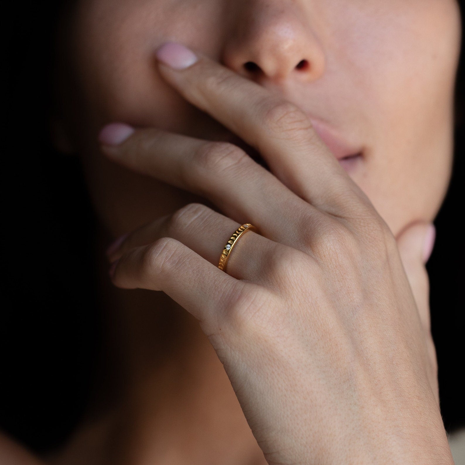 A woman touches her lips, wearing the Augustine Moon Phase Ring—a minimalist piece adorned with small diamonds that subtly channels celestial jewelry.