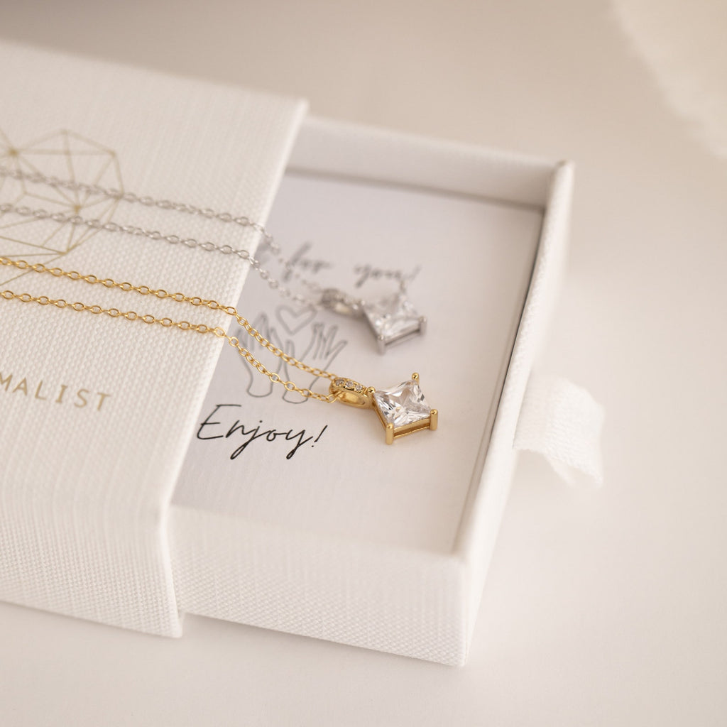 A gold and a silver star-shaped necklace sit atop a white jewelry box with a note, capturing the celestial elegance of the Carina Diamond Necklace.