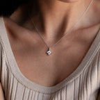 A woman wears the Carina Diamond Necklace—a delicate chain featuring a square diamond pendant—styled with a beige ribbed top.