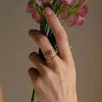 A hand with pink nails holds flowers, wearing two gold rings—a Flower Name Ring and one with script—perfect as a mom gift or for custom flower jewelry lovers.