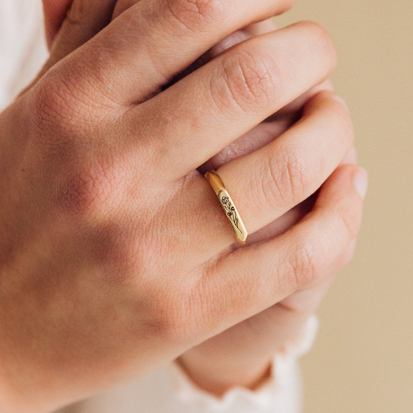 A close-up of a hand wearing the Thin Flower Signet Ring, a gold botanical jewelry piece with a delicate engraved flower design.