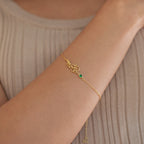 The Flower Birthstone Bracelet, featuring a floral design with a green gem, rests elegantly on a wrist above a beige ribbed top—making it the perfect birthday gift.