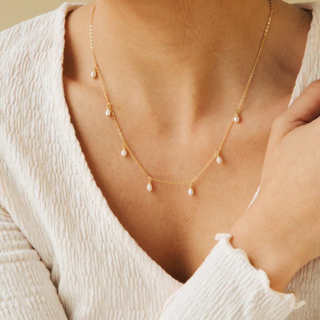 Gold chain necklace with evenly spaced dangling freshwater pearls, worn with a textured white V-neck top.