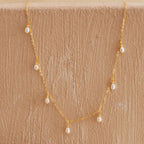 Delicate gold chain necklace with small dangling freshwater pearls, displayed against a textured beige surface.