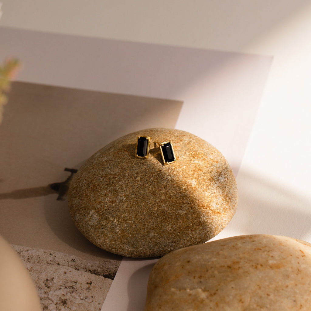 Rectangle Black Onyx Studs featuring rectangular black onyx stones are elegantly displayed on a smooth beige stone, shown in soft natural light.