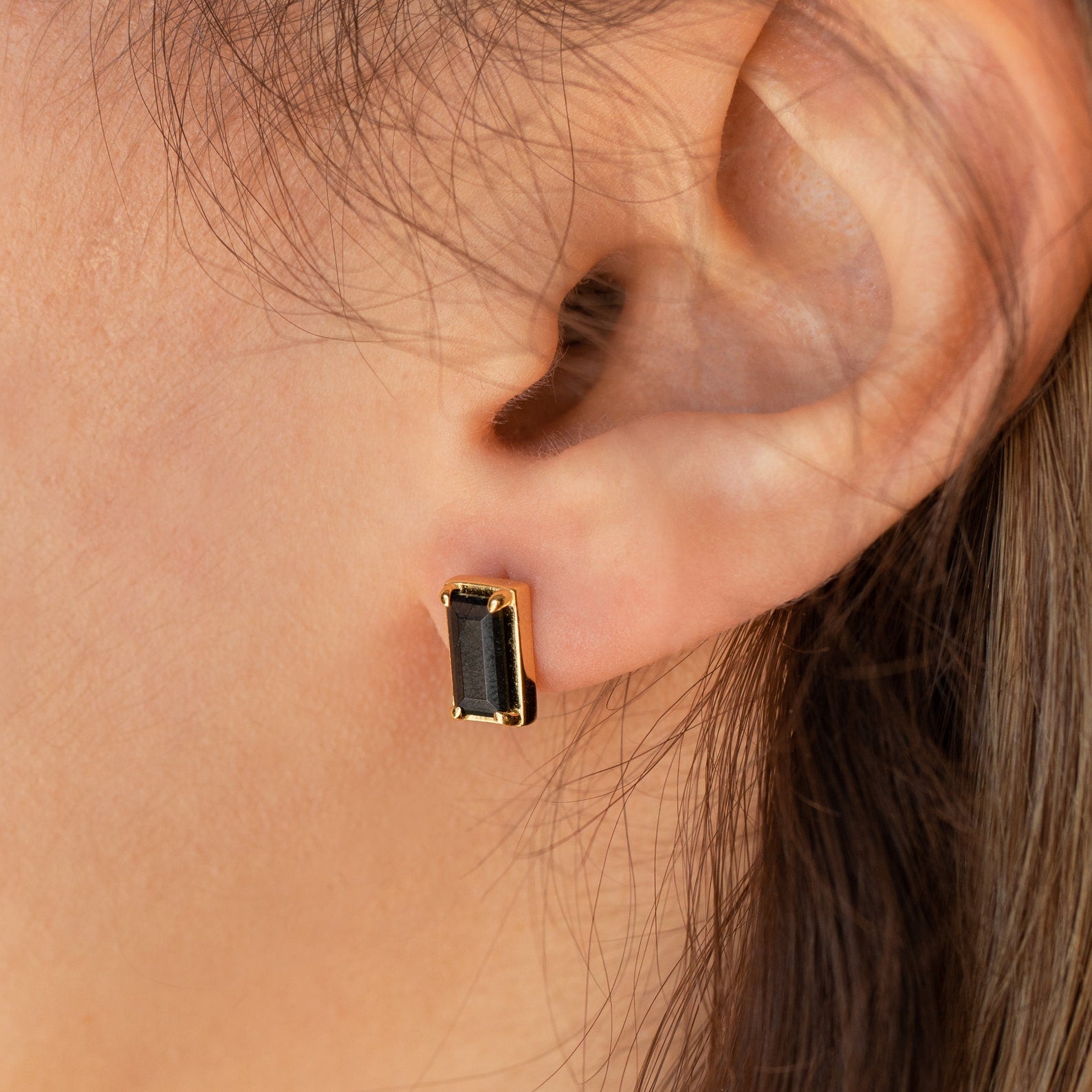 Close-up of an ear wearing Rectangle Black Onyx Studs, showcasing the chic black and gold earrings.