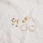 Three pairs of elegant earrings, including hoops and the Rebecca Pearl Drop Earrings, displayed on textured white fabric.
