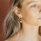A woman with blonde hair wears Rebecca Pearl Drop Earrings—gold hoops featuring a shimmering freshwater pearl drop.