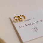 Two Diamond Heart Huggies with sparkling stones rest on a card that reads “Happiness looks beautiful on you”—the perfect dainty hoops to gift someone special.