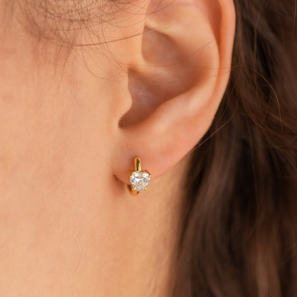 Close-up of an ear with a gold stud earring featuring a round clear gemstone, perfect as a gift or paired with the Diamond Heart Huggies for an elegant, layered look.