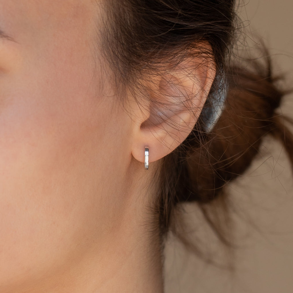 Close-up of a person's ear wearing Editor III Huggies, small silver huggie earrings, with hair tied back—a perfect touch of minimalist jewelry.