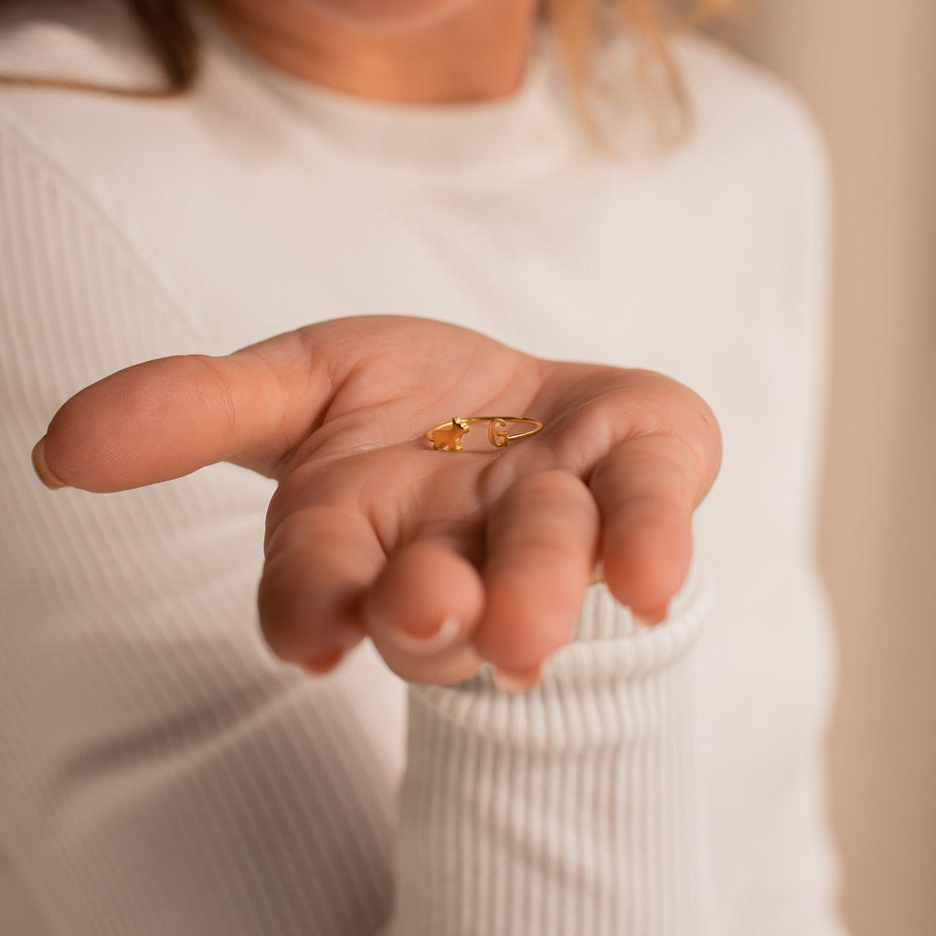 A person in a white top holds the Duo Pet Initial Ring, a small personalized pet jewelry piece, in their open palm with a blurred background.