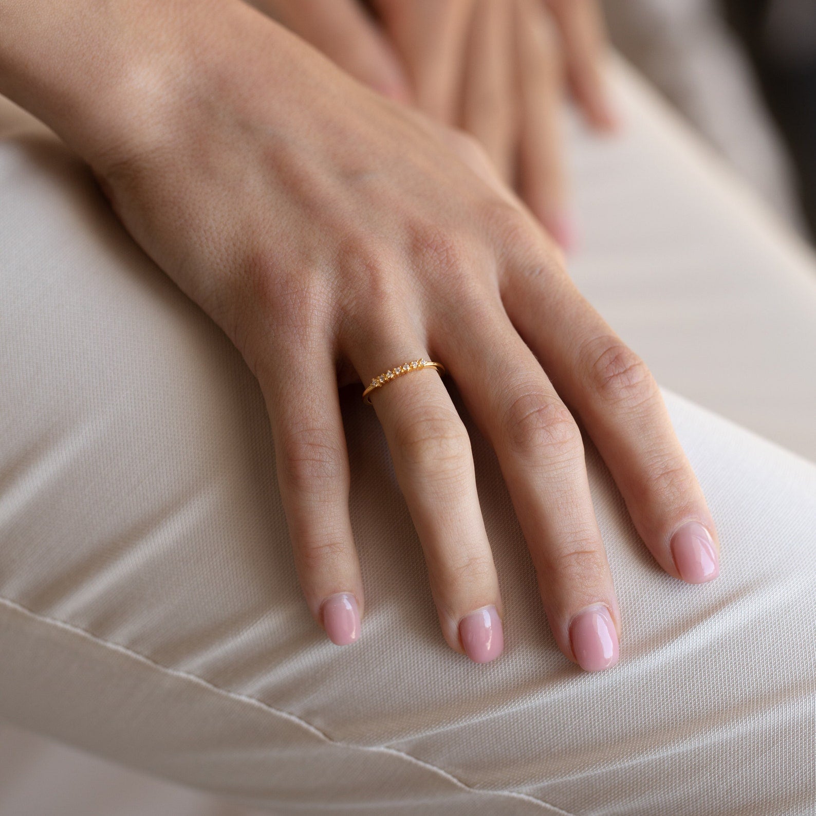 A hand with light pink nails wearing the Isabelle Diamond Ring rests on light-colored pants, highlighting the ring's delicate gold design.