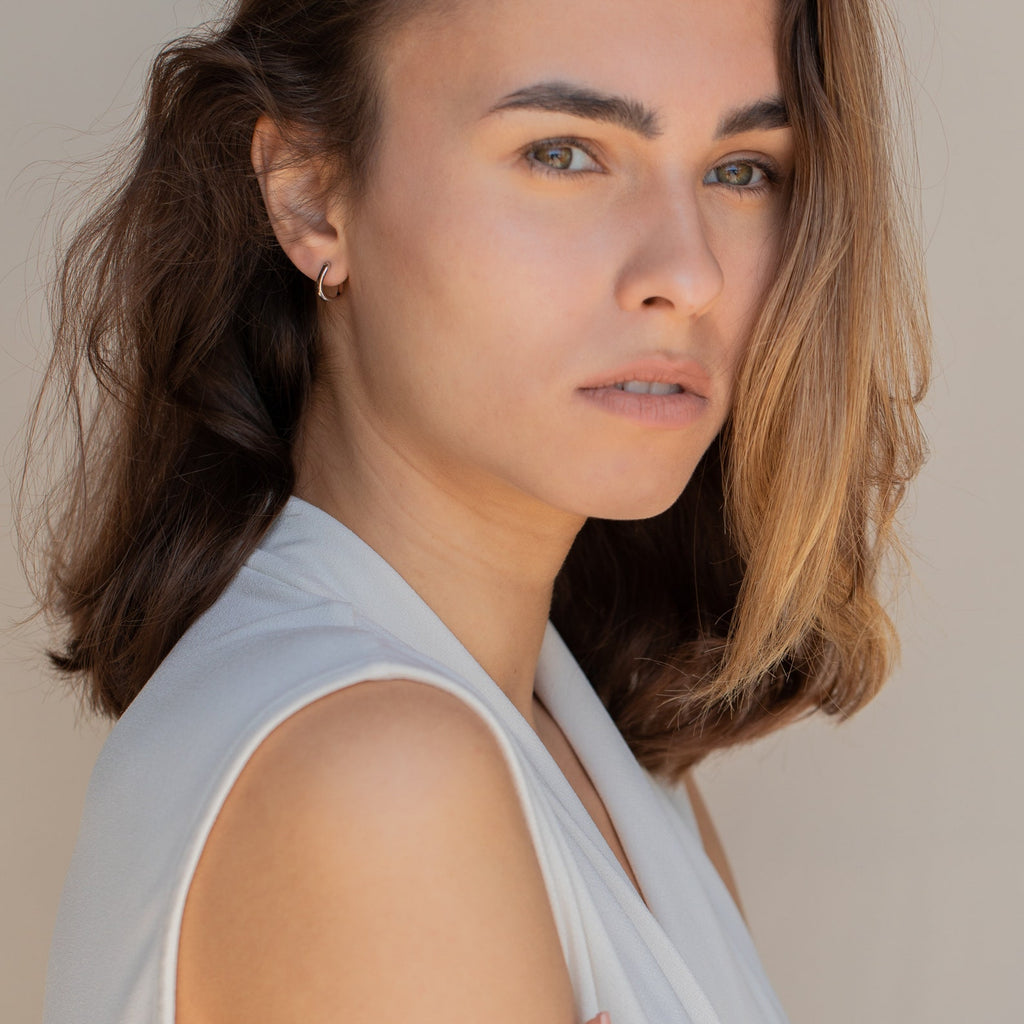 A woman with brown hair wearing a white shirt showcases the McKenna Abstract Hoops, everyday earrings with an organic shape.