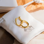 The McKenna Abstract Hoops feature a gold, organic shape and come in a white drawstring pouch with a line drawing of two hands. Effortlessly chic, these modern everyday earrings elevate any outfit.