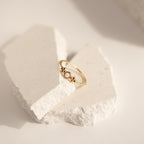 The Sophia Opal Ring is a delicate, vintage-inspired gold ring with a small white opal stone, beautifully displayed on white textured stone pieces.