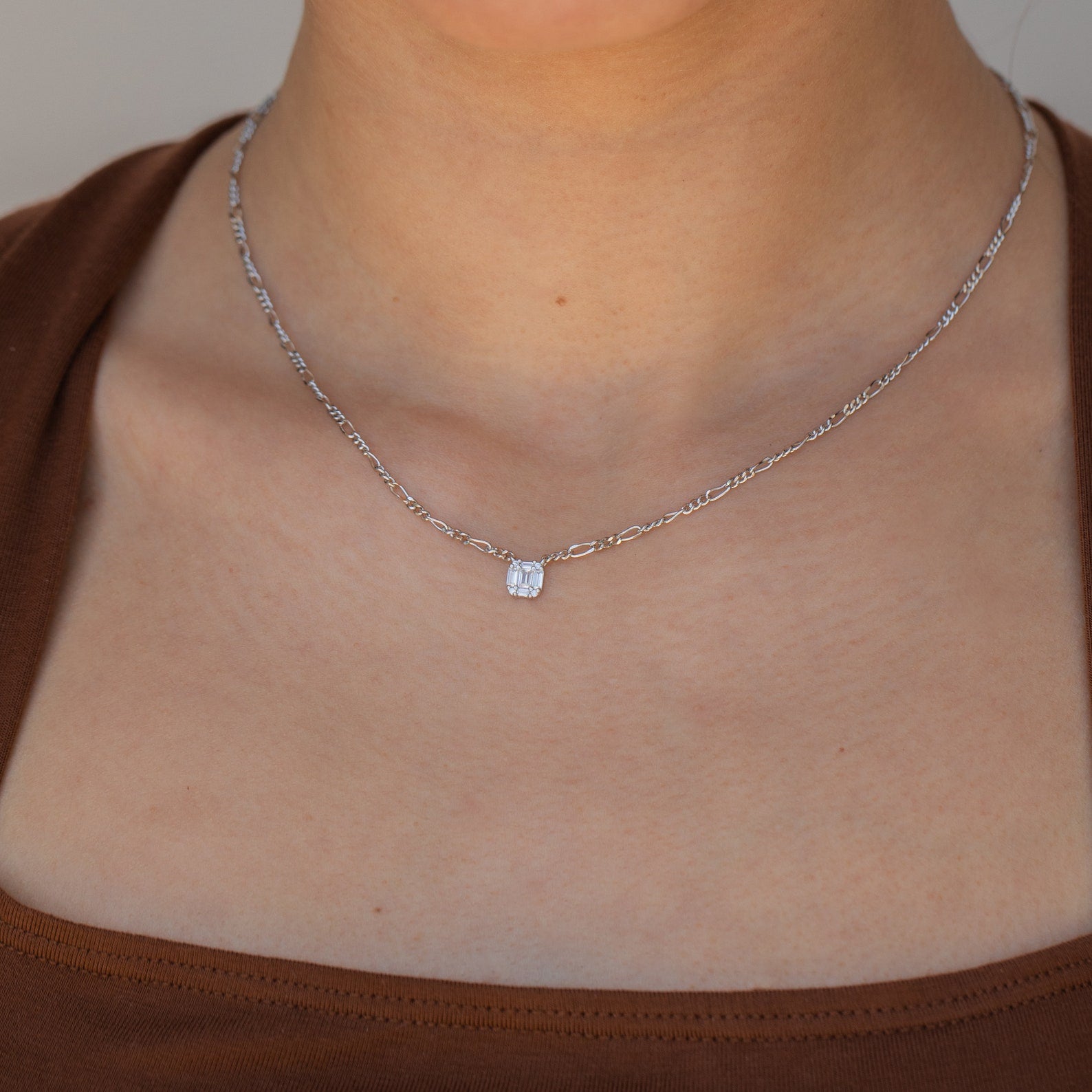 A person wearing the Square Diamond Figaro Necklace with a small rectangular pendant, paired with a brown top.