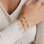 A hand wearing the Malachite Bar Bracelet, featuring green rectangular stones and delicate chain details, rests on a textured white sleeve.