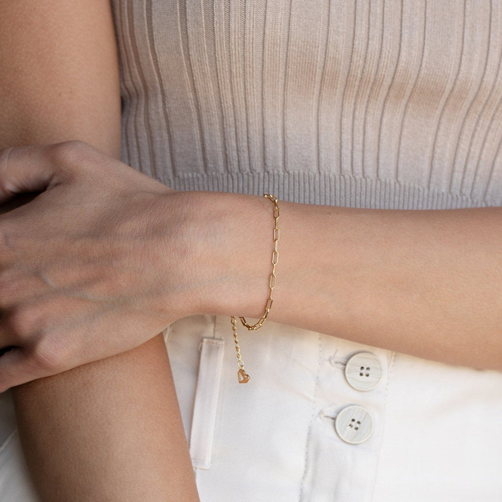 A woman wears a Paperclip Chain Bracelet with a light ribbed top and white pants, arms gently crossed.