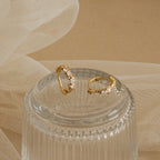 A pair of Sprinkle Diamond Huggies resting on a ribbed glass dish. These small gold hoop earrings are adorned with a scattered arrangement of variously shaped diamond CZ stones, including marquise, round, and oval cuts.