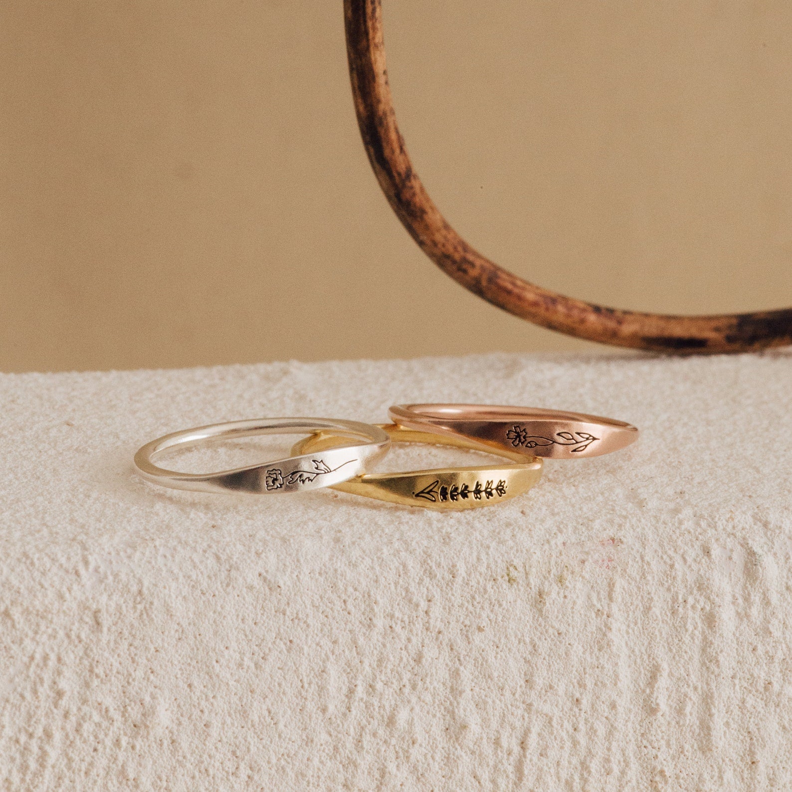 The Skinny Flower Ring is shown in silver, gold, and rose gold on a textured surface. This botanical jewelry adds delicate elegance to any look, making it a perfect unique accent.
