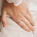 A hand wearing the gold Flower Bar Ring rests on a hip, paired with light beige pants and a textured white top.