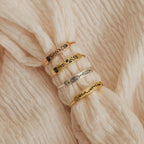 Four engraved metal bracelets with botanical designs, perfect for stacking with your favorite skinny band or the Flower Bar Ring, displayed on soft cream knit fabric. This botanical jewelry adds a delicate touch to any look.