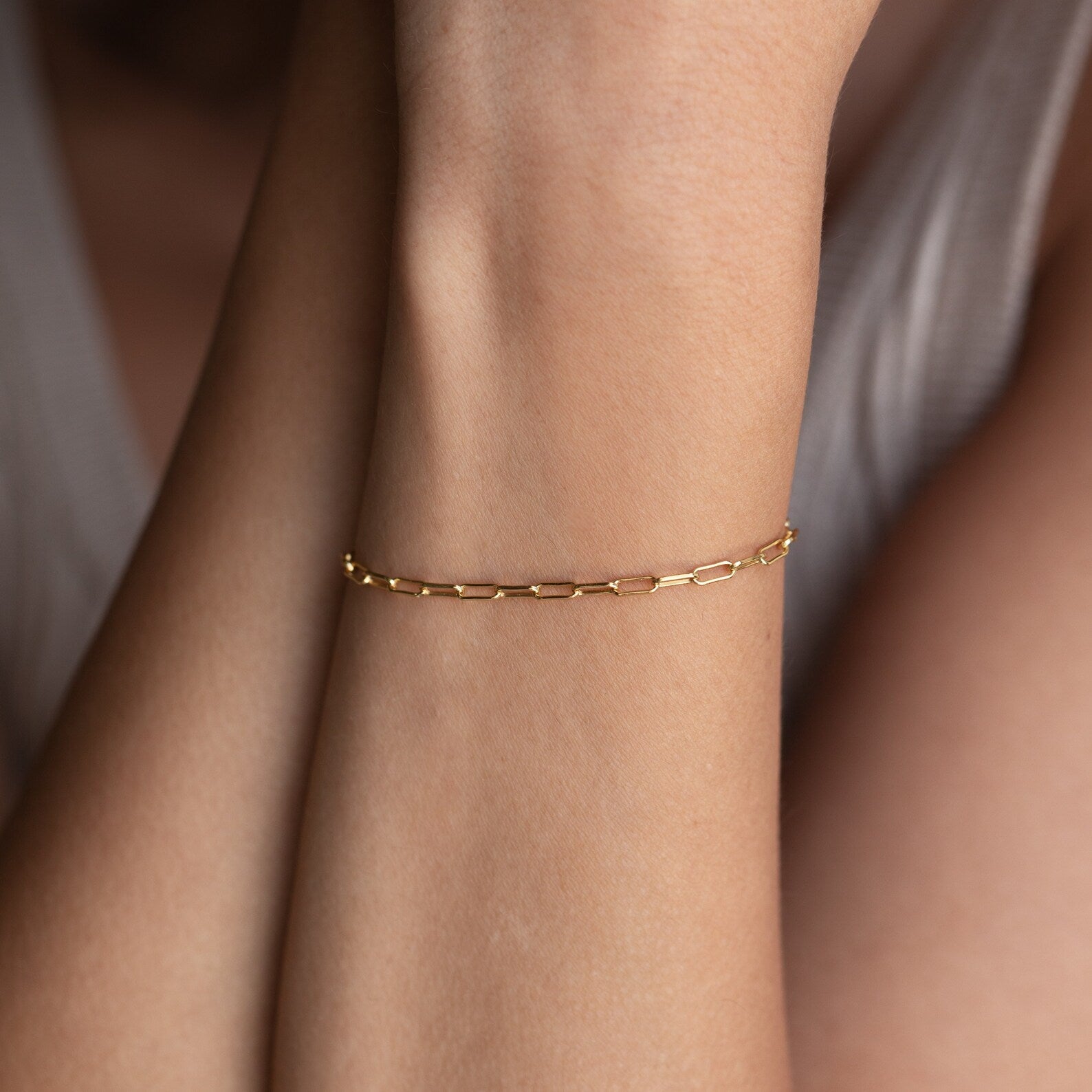 The Paperclip Chain Bracelet graces a wrist with arms gently crossed and a white top—perfect for effortless stacking.