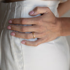 A hand adorned with the Augustine Moon Phase Ring rests on the hip of someone in white high-waisted pants.