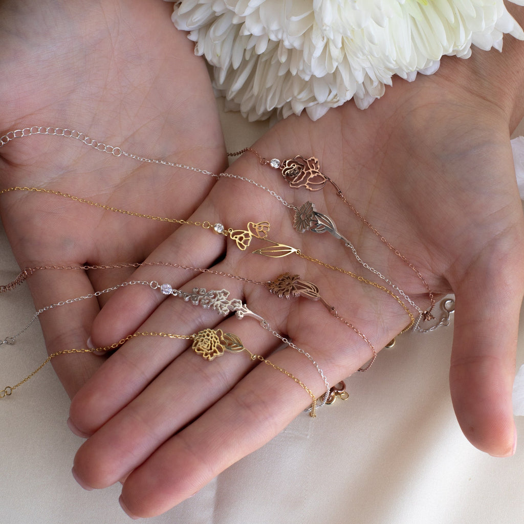 A hand displays several Flower Birthstone Bracelets in gold, silver, and rose gold tones—ideal as a birthday gift or thoughtful keepsake.