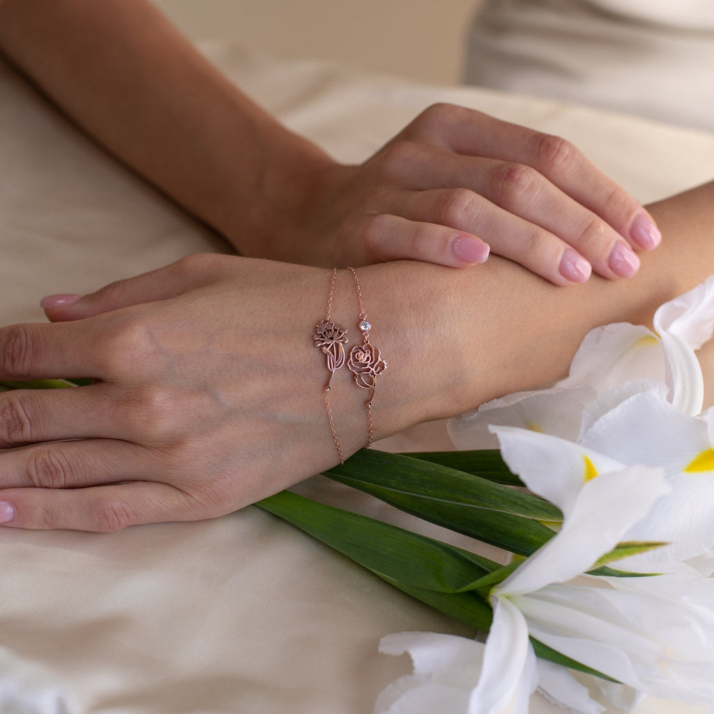 A woman's hands with a rose gold Flower Birthstone Bracelet rest on satin beside white lilies, creating a thoughtful birthday gift.