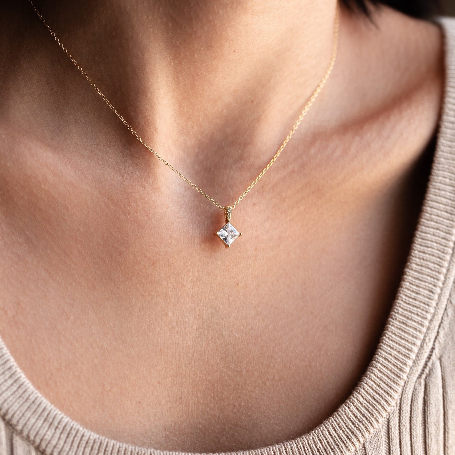 Close-up of a woman wearing the Carina Diamond Necklace, which showcases a gold chain and a sparkling square diamond pendant.