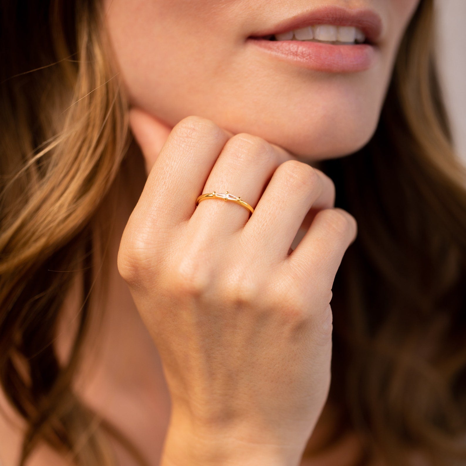 A woman with loose wavy hair touches her chin, wearing the elegant Eleanor Baguette Diamond Ring on her finger.