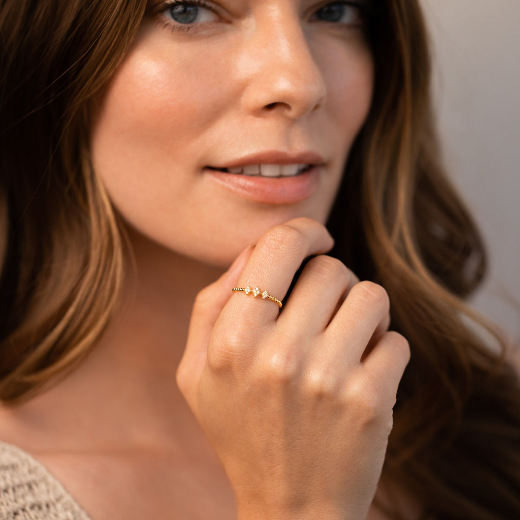 A woman with long brown hair smiles softly, displaying the Jasmine Beaded Diamond Ring with small sparkling stones as part of her chic ring stack.