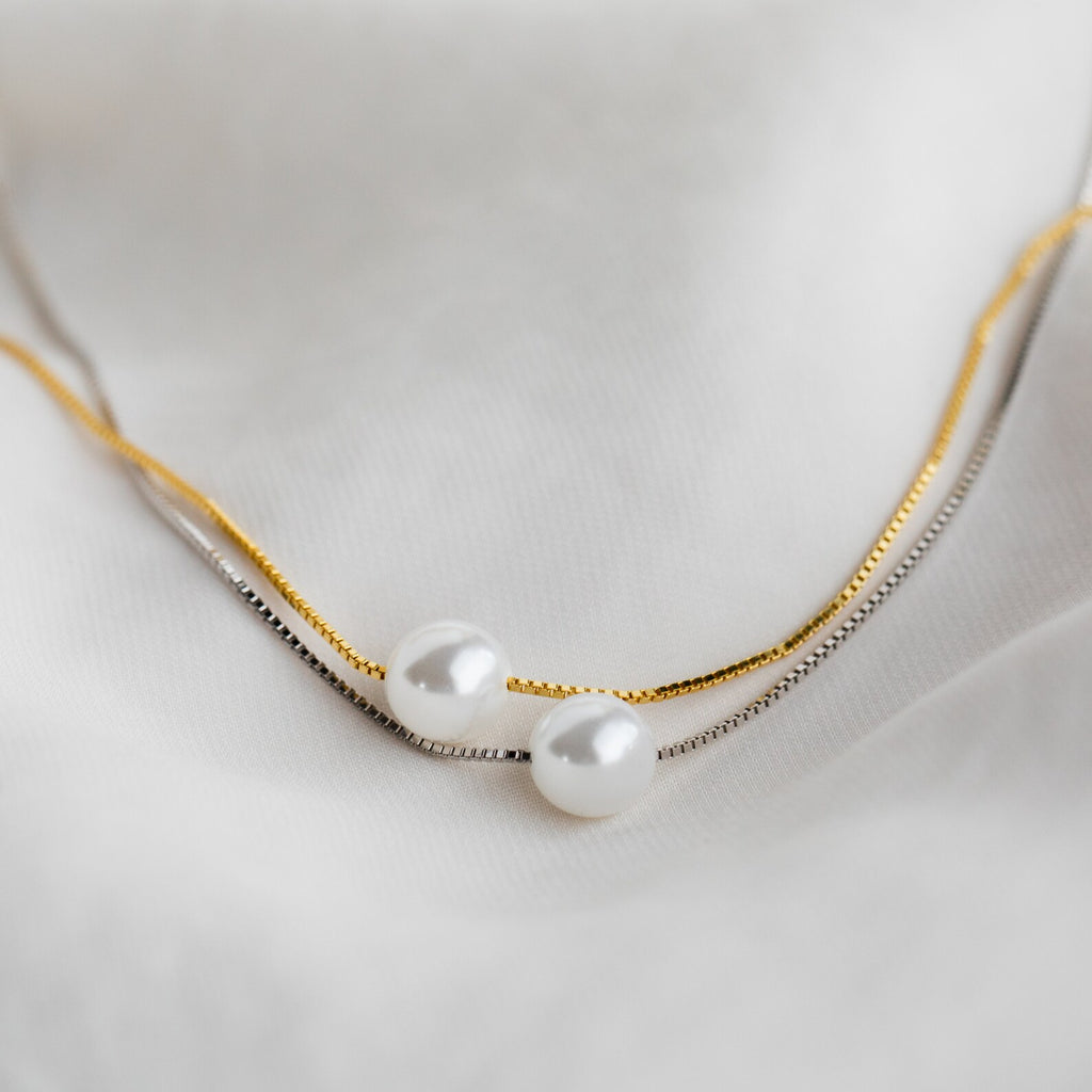 The Kennedy Pearl Necklace, available in gold and silver, is elegantly displayed on soft white fabric—perfect minimalist jewelry for any wedding collection.