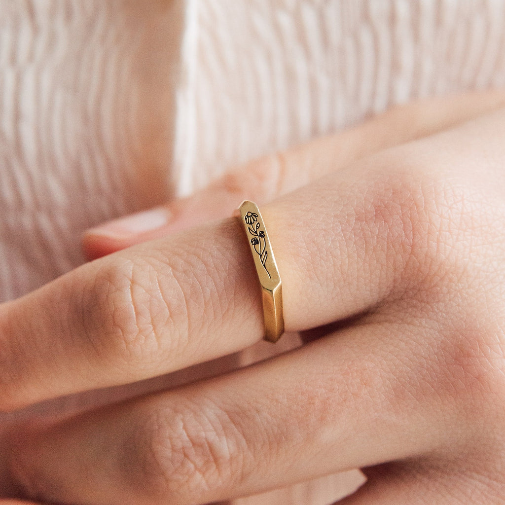 A hand wears the Thin Flower Signet Ring, a gold personalized pinky ring with a delicate engraved floral design—ideal for botanical jewelry lovers.